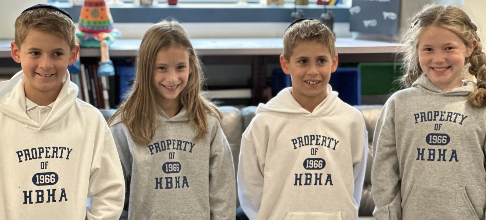 Four young HBHA students smile in matching gray or white sweatshirts that say: Property of HBHA (1966)