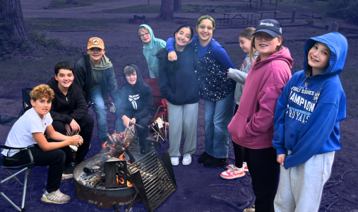 students smiling around a campfire on the 6th-grade camping trip